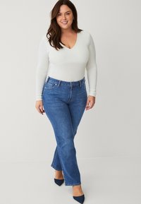 Witte lange mouwen body suit en blauwe straight-leg jeans, met een middelhoge taille, minimale slijtage en spitse marineblauwe schoenen.