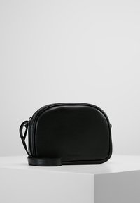 Borsa a tracolla nera in pelle con una forma arrotondata, chiusura a zip e spallaccio rimovibile. Texture liscia con dettagli minimi.