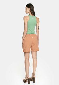 Zielony prążkowany top na ramiączkach z srebrnym akcentem, w połączeniu z pomarańczowymi szortami z troczkiem w talii i podwiniętymi nogawkami. Brązowe sandały na obcasie.