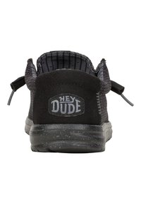Schwarze lässige Schuhe mit einem strukturierten Obermaterial, abgerundetem Schaftrand und einer grauen Gummisohle, die das Logo "HEY DUDE" an der Ferse zeigt.