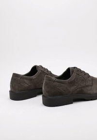 Un par de zapatos de gamuza gris oscuro con cordones y suelas de goma negra gruesa sobre un fondo claro.