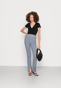 Top preto em tecido envolvente, calças de cintura alta azul e branca com padrão xadrez e fendas frontais, e bolsa preta. Textura suave, design justo.