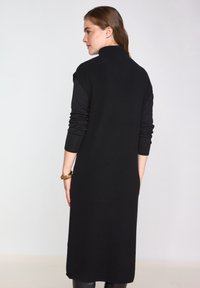 Abito nero in maglia con colletto alto, maniche lunghe e silhouette dritta, realizzato in un tessuto texture e design minimalista.