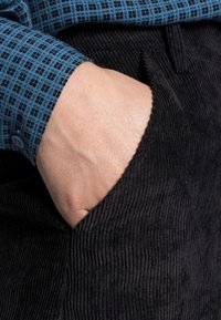 Niebieska koszula w kratę z zapięciem na guziki, zestawiona z czarnymi spodniami z kordurowej tkaniny, które mają boczną kieszeń. Teksturowany i dopasowany fason.