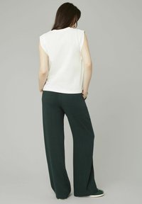 Un haut sans manches blanc avec un col rond associé à un pantalon large, vert foncé, présenté de dos sur fond neutre.