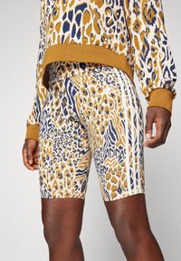 Leopardmönstrade shorts i beige, guld och marinblå, med vita ränder på sidorna och en åtsittande design. Mjuk tyg med intrikata mönster.