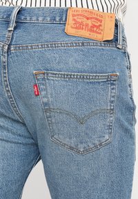 Modré džíny z denimu s koženým zadním štítkem, rovný střih, viditelné švy a červená cedulka Levi's na zadní kapse.