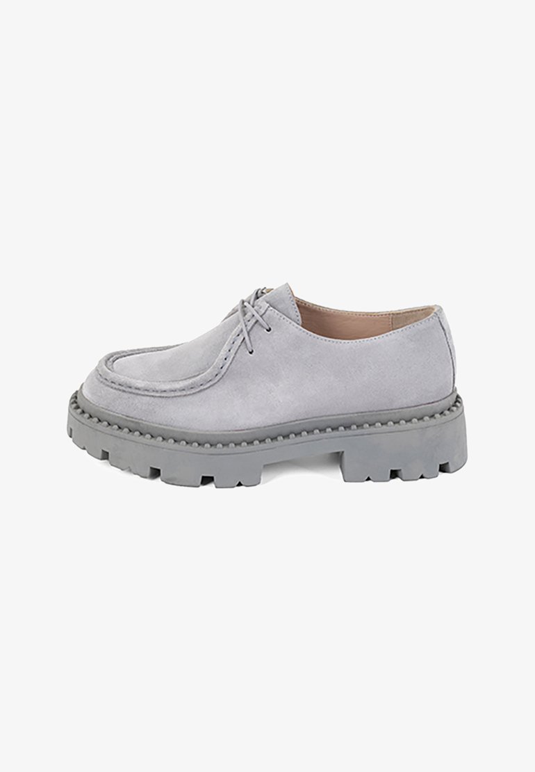 Chaussure en suede gris à lacets avec un bout rond, semelle épaisse texturée et piqûres contrastantes le long du bord supérieur.