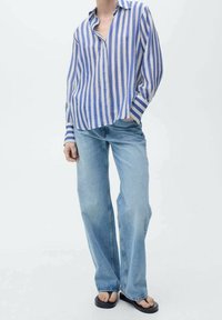 Chemise à manches longues rayée bleu et blanc avec une coupe décontractée, associée à un jean pattes larges bleu clair et des tongs noires. Design simple et décontracté.