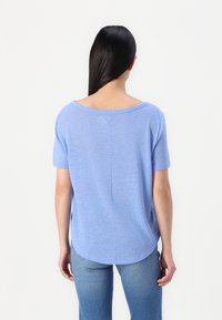 Top scurt de culoare albastră deschisă, cu un croi relaxat și guler rotund. Material moale cu o textură subtilă, prezentând o cusătură centrală pe spate.