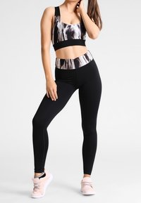 Czarne legginsy w połączeniu z crop topem o wzorze, który łączy czarne i białe kolory. Top posiada szeroki, jednolity czarny pas.