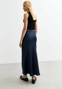 Jupe maxi en satin bleu marine avec une texture lisse, dotée d'une taille ajustée et d'un ourlet évasé. Associée à un crop top noir à côtes et des chaussures à enfiler.