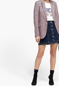 Czerwona i biała kraciasta marynarka na białym t-shircie z grafiką, zestawiona z dżinsową spódnicą w linii A zapinaną na guziki z przodu. Całość dopełniają czarne skarpetki do kostek.