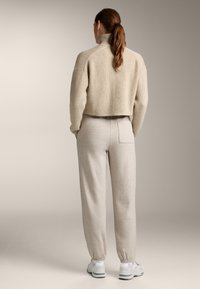 Beige gerippter Strickpullover mit hohem Kragen, kombiniert mit hellbeigen Sweatpants mit elastischen Bündchen und einer Gesäßtasche. Sportliche Sneaker.