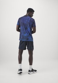 Camiseta deportiva azul con un patrón de líneas en espiral, combinada con pantalones cortos negros y zapatillas negras, mostrando un diseño texturizado y un ajuste moderno.