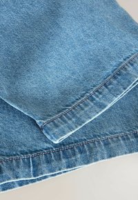 Le tissu en denim bleu présente une texture lisse avec un léger éclat. Les bords finis ont des coutures de contraste, mettant en valeur un design plié.