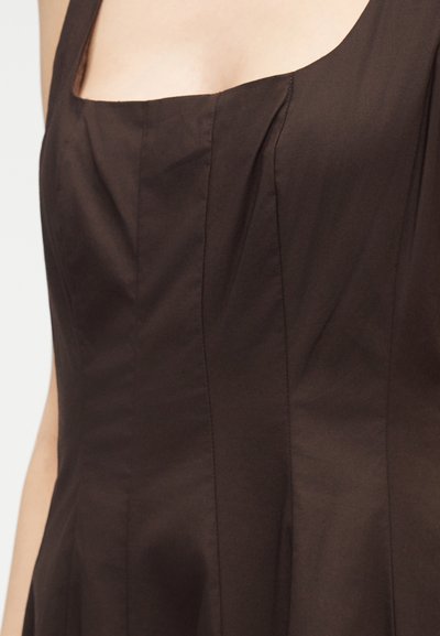 Κοντινό πλάνο ενός καφέ αμάνικου φορέματος με τετράγωνη λαιμόκοψη και κάθετες ραφές στο μπούστο.