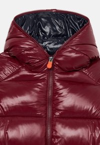 Burgunderfarbene glänzende Pufferjacke mit schwarzem Innenfutter und zentralem Reißverschluss mit einem orangefarbenen Anhänger.