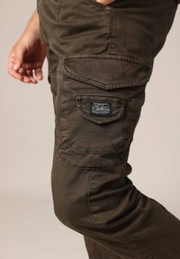 Olijfgroene cargo broek van een duurzaam katoenmix, met meerdere zakken, versterkte stiksels en een geborduurd logo op de achterzak.