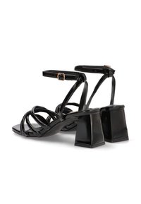 Sandalias negras de tiras con un acabado brillante, que cuentan con un tacón cuadrado, correa en el tobillo con hebilla y un intrincado diseño trenzado en la parte superior.