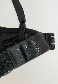 Soutien-gorge en dentelle noire avec bretelles ajustables, une bande texturée et une fermeture à plusieurs crochets avec quincaillerie en métal pour un ajustement personnalisé.