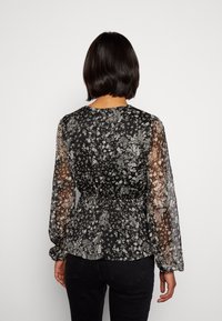 Czarna bluzka w kwiaty z przezroczystymi długimi rękawami i dopasowanym w pasie krojem. Charakteryzuje się delikatnym wzorem drobnych białych kwiatów na tkaninie.