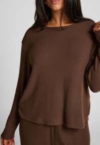 Bruine geribde lange mouw top met een relaxte pasvorm, met een ronde halslijn en brede mouwen, gemaakt van zachte stof met gestructureerde lijnen.