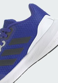 Scarpa sportiva blu con motivo e dettagli neri, dotata di una tomaia in tessuto testurizzato e di una suola bianca sagomata con design antiscivolo.