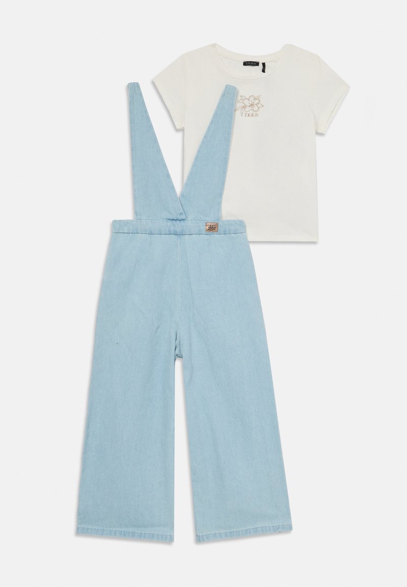 Salopetă din denim de culoare albastru deschis, cu picioare largi și bretele reglabile, asociată cu un tricou alb cu un design floral și logo.