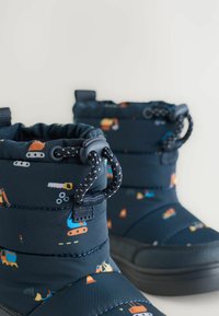 Blå vinterstøvler med polstret design, elastisk snøring og farverige mønstre med bygge temaer på stoffet. Tekstilart sort sål.