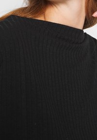 Black ribbed sweater with a high neckline. The textured fabric features vertical stripes, creating a structured look.