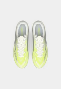 Φωτεινά κίτρινα και γκρίζα ποδοσφαιρικά παπούτσια με κομψό σχέδιο, υφασμάτινη επιφάνεια, επίπεδες κορδόνες και σήμανση στα πλάγια.