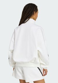 White oversized sweatshirt with a high collar, featuring elastic cuffs and a smooth texture. Black accents along the sides add contrast.