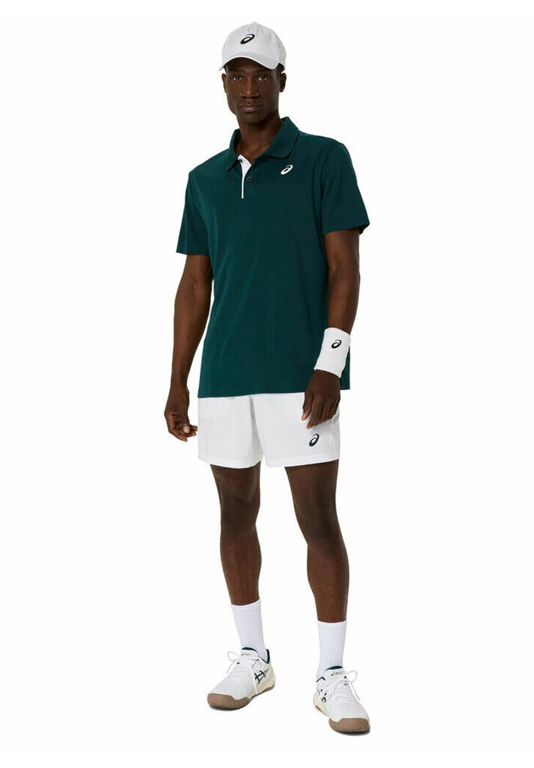 Polo shirt verde scuro con accenti bianchi, pantaloni corti bianchi, fascetta, cappellino bianco e scarpe da ginnastica con suola chiara e accenti scuri.