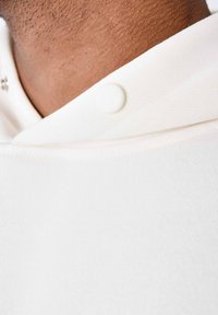 Witte hoodie met een ronde hals en knoopsluiting. De stof lijkt glad met een fijne textuur en heeft minimalistische ontwerpinformatie.