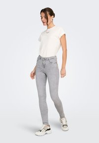 Ανοιχτό γκρι στενά τζιν παντελόνια συνδυασμένα με λευκό κοντομάνικο μπλουζάκι και λευκά αθλητικά παπούτσια με μαύρες λεπτομέρειες, με απλό σχέδιο και απαλή υφή.