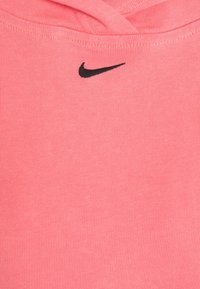 Růžová sportovní tkanina s žebrovanou strukturou, se malým černým logem Nike umístěným ve středu blízko výstřihu.