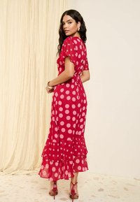 Punainen pilkullinen midi-mekko, jossa on lyhyet hihat, kerroksellinen röyhelöhelma ja kootut vyötärö. Läpinäkyvä pinta; täydentää punaiset korkokengät.