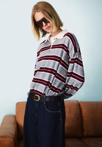 Sivi in maroon prugasti dolg rokav polo s kragnico, v paru z temnimi denim hlačami in rjavim pasom. Nošene črne sončna očala.