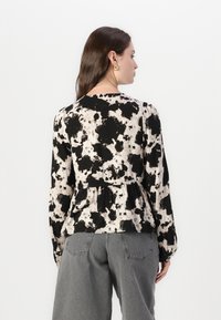 Peplum bluza u crnoj i bež boji s točkastim uzorkom; dugi rukavi i okrugli izrez; uparen s visokim sivoim hlačama.