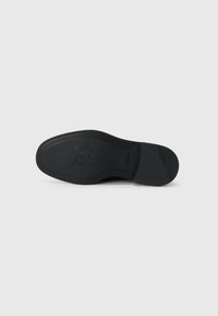 Semelle de chaussure en cuir noir avec une texture lisse, présentant un motif décoratif et un logo imprimé. Bords courbés et zone de talon arrondie.