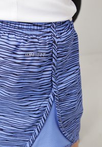 Shorts de sport bleus avec un motif rayé, fabriqués en tissu léger avec des accents en maille. Comprend un logo Dri-Fit sur le côté.