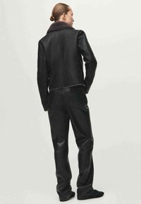Czarna skórzana kurtka z kołnierzem z kożucha, dopasowanym krojem i widocznymi szczegółami przeszyć, zestawiona z pasującymi czarnymi skórzanymi spodniami.