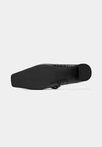 Chaussure en cuir noir avec une finition lisse et un motif en croco texturé. Dotée d'une semelle plate et d'un design à bout pointu.