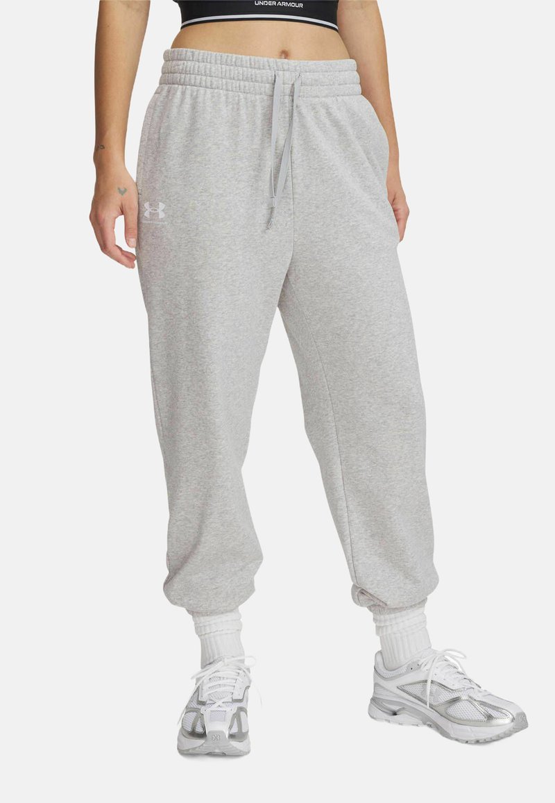 Grijze sweatpants met een elastische tailleband en een trekkoord. Heeft een taps toelopende broekspijpen en zijzakken. Gekoppeld met witte sneakers en sokken.