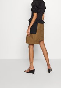 Schwarzes Top mit puffärmeln und Rüschensaum, kombiniert mit einem beigefarbenen Rock, der einen großen schwarzen Patch aufweist. Wedgesandalen runden das Outfit ab.