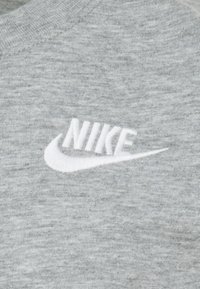 Siva tkanina od dukserice z mehkimi vlakni ima na sprednji strani vezeno belo Nike logo.