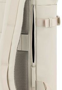 Bolso de color crema con un acabado de tela texturizada, que presenta una abertura con cremallera, correas ajustables y una hebilla lateral para el cierre.