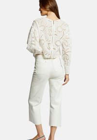 Haut en dentelle blanche avec des motifs découpés élaborés, manches bouffantes et fermeture éclair au dos, associé à un pantalon cropped blanc.