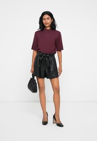 Burgundy bordás kötött felső, fekete műbőr sort, megkötős övvel, fekete magassarkú cipő és egy kis fekete kézitáska. Egyszerű és modern dizájn.